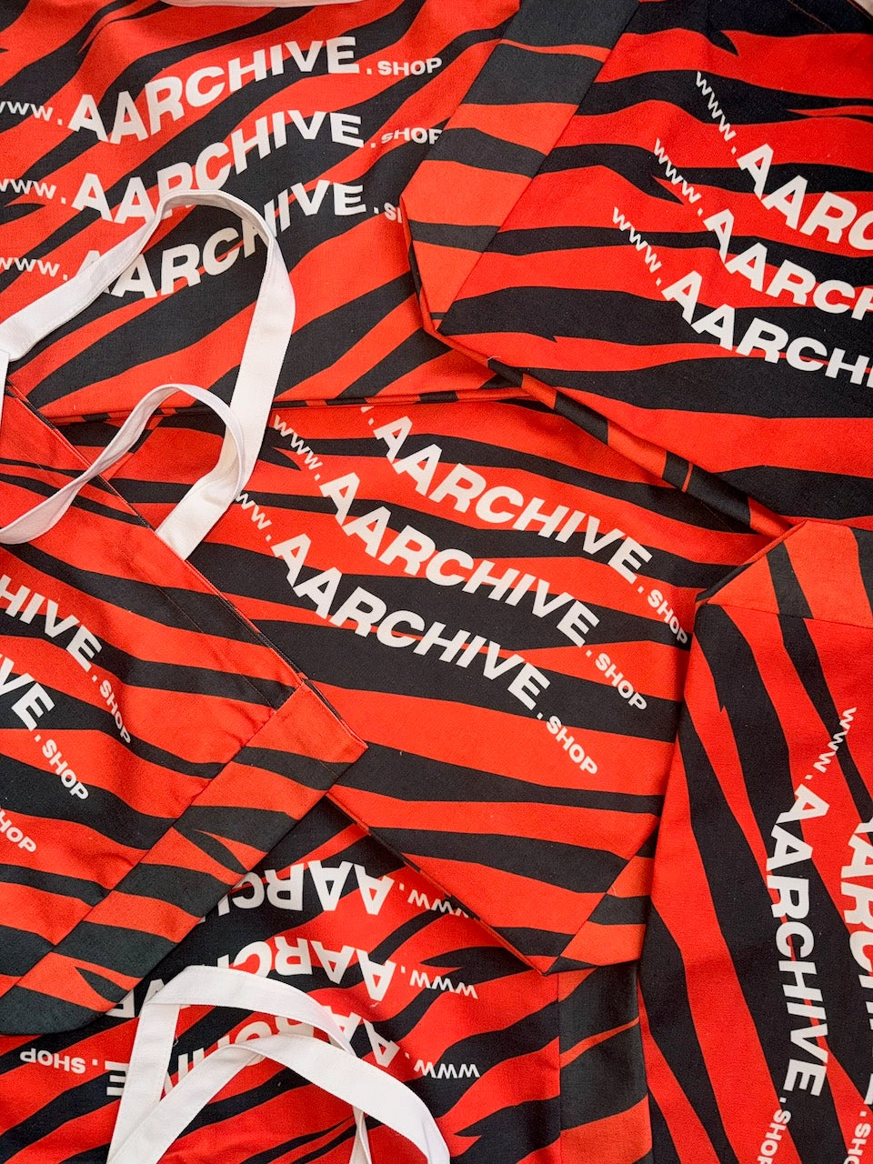 A group of red and black striped AARCHIVE tote bags with white handles